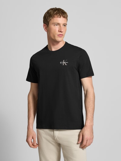 Männermodel trägt T-Shirt mit Rundhalsausschnitt und Logo von Calvin Klein Jeans, schwarze Reine Baumwolle, Regular-Fit, Nahaufnahme Oberkörper. Rückenlänge bei Größe M: 69 cm.
