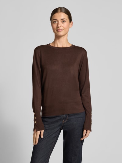 Modelka nosi brązowy Strickpullover aus Viskose-Mix Modell 'KATIE' od FREE/QUENT, krój regular fit, okrągły dekolt, guziki na rękawie, długość tyłu w rozmiarze S: 51 cm, długość rękawa w rozmiarze S: 63 cm, kolor gładki, przód z widoczną teksturą dzianiny, pełny widok sylwetki z przodu.