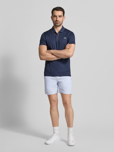 Męski model nosi Loose Fit Sport-Shorts mit Mesh-Bund od Lacoste, jednokolorowy efekt, wyhaftowane logo, tunel, elastyczny siateczkowy pas, wpuszczane kieszenie, zdjęcie całej sylwetki z przodu.