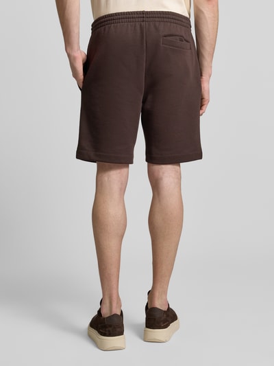 Männermodel trägt Regular Fit Sweatshorts aus Baumwoll-Mix von Lacoste, unifarben braun, elastischer Bund, seitliche und Gesäßtaschen, Ganzkörperansicht Rückansicht.