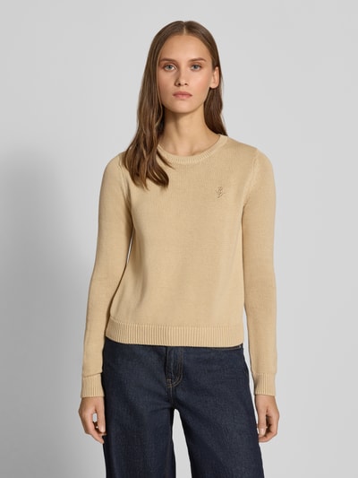 Frauenmodel trägt Slim Fit Pullover aus reiner Baumwolle von REVIEW, beige Farbe, Strick-Optik, Logo-Stitching, Nahaufnahme Oberkörper.