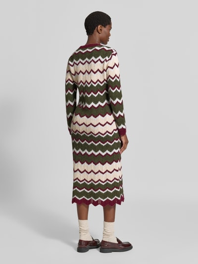 Frauenmodel trägt Strickkleid in Midilänge von miss goodlife in Grün, Creme und Bordeaux mit Muschelsaum, Langarm, Ganzkörperansicht Rückansicht.