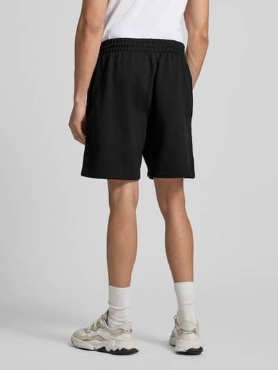 Männermodel trägt Regular Fit Sweatshorts aus Baumwoll-Mix Modell 'TREFOIL ESSENTIALS' von adidas Originals in Optik: Unifarben, Logo-Stitching, elastischer Bundabschluss, seitliche Eingrifftaschen, Materialverarbeitung: Sweat, Ganzkörperansicht Rückansicht.