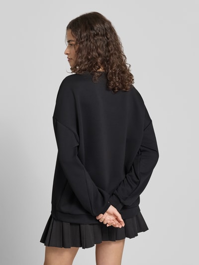 Frauenmodel trägt schwarzen Relaxed Fit Pullover mit Herz-Stickerei Modell 'TALIA' von Pieces, unifarben, langarm, Rundhals, Ganzkörperansicht Rückansicht