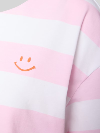 Vrouwenmodel draagt Pyjama-Oberteil met Motiv-Print van Mey, roze-witte strepen, oranje smiley, zachte stof, detailopname schouder.