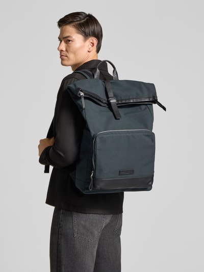 Männermodel trägt Rucksack mit Rolltop und Laptopfach von MARC O'POLO in Dunkelgrün mit Label-Prägung, Reißverschlüssen und Baumwollstruktur, Ganzkörperansicht Rückansicht.