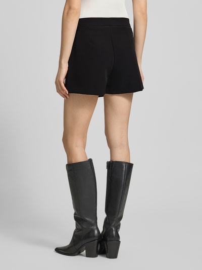 Frauenmodel trägt Regular Fit Minirock mit integrierter Shorts Modell 'Sofia' von JJXX in Schwarz, glatte Textur, Ganzkörperansicht Rückansicht, Damen Minirock, elastischer Material-Mix, Wickel-Optik.