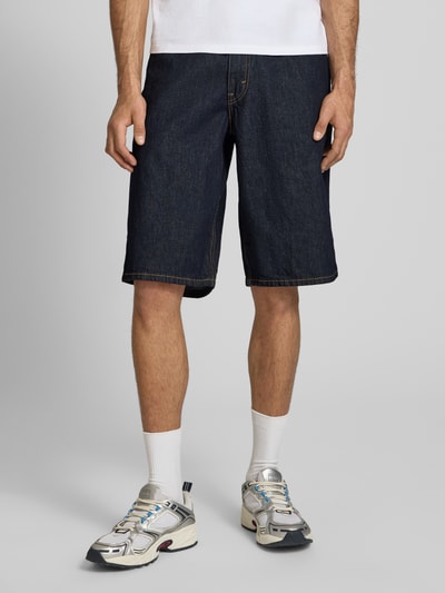 Männermodel trägt Baggy Jeansshorts aus reiner Baumwolle Modell '470' von Levi's®, dunkelblaue Denim-Optik, 5-Pocket-Design, Nahaufnahme Beine.