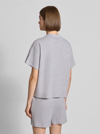Frauenmodel trägt Relaxed Fit Poloshirt mit Strukturmuster Modell 'Noa' von OH APRIL in Hellgrau, strukturierte Oberfläche, Ganzkörperansicht Rückansicht. Damen Poloshirt von OH APRIL, Relaxed Fit, Strukturmuster, Knopfleiste, Rückenlänge bei Größe S: 55 cm.