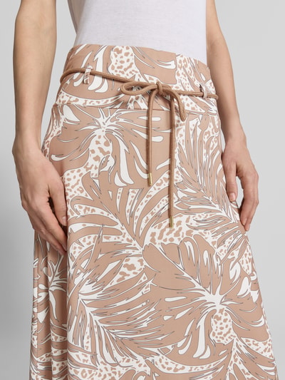 Frauenmodel trägt Midirock im Allover-Look mit Bindegürtel von More & More in Beige mit weißen tropischen Mustern, Nahaufnahme Oberkörper.