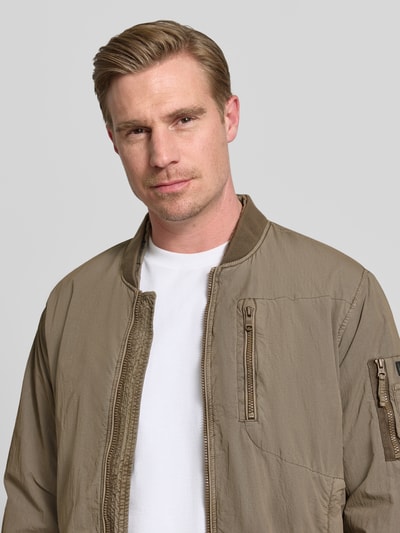 Männermodel trägt Blouson mit Label-Patches Modell 'IBE' von khujo in Beige, Reißverschluss, Reißverschlusstasche, Nahaufnahme Oberkörper. Gerader-Schnitt, kurzer Stehkragen, Brusttasche mit Reißverschluss, Ärmel-Reißverschlusstasche, seitliche Eingrifftaschen, Maße: Rückenlänge 64 cm, Schulterbreite 48 cm, Brustweite 56 cm, Ärmellänge 62 cm.