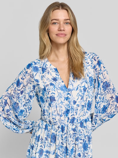 Frauenmodel trägt Midikleid aus reiner Viskose mit floralem Allover-Print von ROBE LÉGÈRE, Tailliert, Tunika-Ausschnitt, Langärmelig, Knopfleiste, Nahaufnahme Oberkörper. Rückenlänge bei Größe 36: 123 cm, Brustweite 49 cm, Ärmellänge 60 cm. Blau-weiße Farben, leichte Stofftextur.