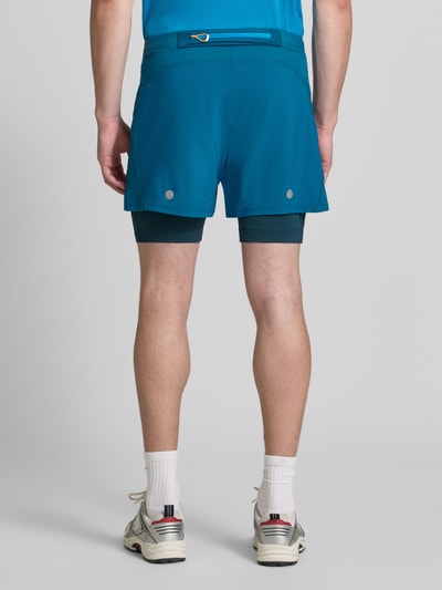 Männermodel trägt Regular Fit Shorts mit integrierten Tights Modell 'Road' von ASICS TIGER, türkis, glattes Material, elastischer Bund, Logo-Detail, Szerokość w rozmiarze M: 38 cm, Długość wewnętrzna nogawki: 12 cm, Ganzkörperansicht Rückansicht.