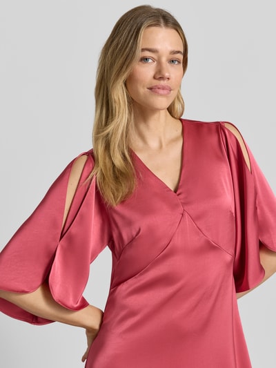 Vrouwenmodel draagt dames midi-jurk van satijn in roze met V-hals, vlindermouwen, straight fit, model 'Remara' van Neo Noir, detailopname bovenlichaam. Ruglengte maat 36: 109 cm, borstwijdte: 47 cm, mouwlengte: 38 cm.