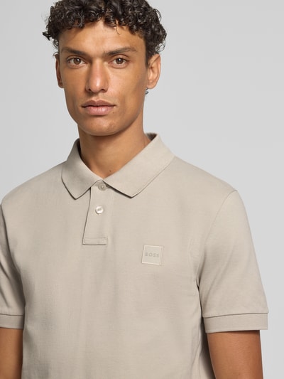Męski model nosi Slim Fit Poloshirt aus Baumwoll-Mix od BOSS Orange, efekt: jednolity kolor, naszywka z logo, kołnierzyk polo, rękaw: krótki rękaw, zakończenie rękawów: prążkowane, wykończenie materiału: pika, mieszanka bawełny, Nahaufnahme górnej części ciała.