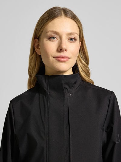 Frauenmodel trägt Regular Fit Mantel mit Stehkragen Modell 'Suva' von Rains in Schwarz, glatte Textur, Nahaufnahme Oberkörper, taillierte Passform, abnehmbares Stoffband, Pattentaschen, Rückenlänge bei Größe S 113 cm, Schulterbreite 42 cm, Brustweite 51 cm, Ärmellänge 62 cm.