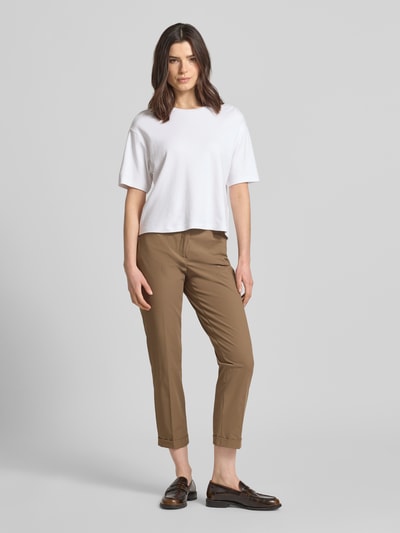 Frauenmodel trägt Chino aus Techno Cotton Superstretch Modell 'UTE' von Raffaello Rossi in Camel, mit Bügelfalten, Eingriffstaschen, fixierten Beinumschlägen, Gürtelschlaufen, Knopf- und Reißverschluss, Elastischer-Material-Mix, Straight Fit, verkürzte Passform, Ganzkörperansicht von vorne.