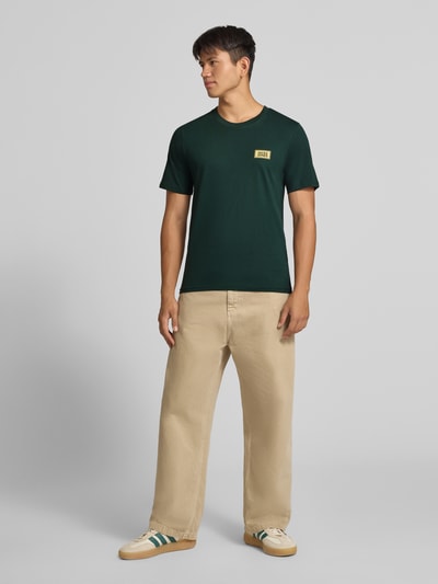 Männermodel trägt Regular Fit T-Shirt aus reiner Baumwolle mit Label-Detail von JACK & JONES, Rundhalsausschnitt, Beige Hose, Ganzkörperansicht von vorne.