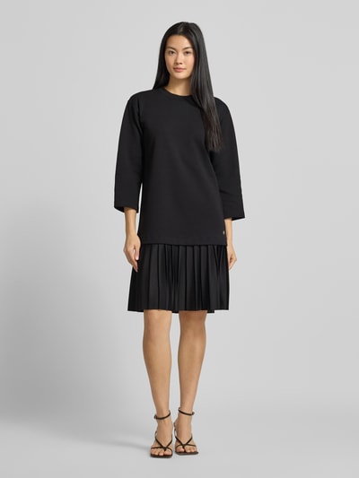 Frauenmodel trägt sukienkę do kolan w efekcie 2 w 1 model 'Tarika' od JOOP!, krój relaxed fit, okrągły dekolt, rękaw o dł. 3/4, kolor czarny, faktura gładka z plisowanym dołem, całkowita długość tyłu 95 cm, szerokość klatki piersiowej 51 cm, długość rękawów 46 cm, całkowita długość do kolan, ganzkörperansicht von vorne.