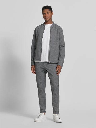 Męski model nosi Slim Fit Hose mit Viskose-Anteil in verkürzter Passform od Lindbergh z elastycznej mieszanki wiskozy, skrócony krój slim fit, wpuszczane kieszenie, kieszeń z tyłu, zapięcie na guzik i zamek błyskawiczny, szerokość w rozmiarze M: 42 cm, długość wewnętrzna nogawki: 72 cm, odcień szarości, faktura gładka, całkowity widok z przodu