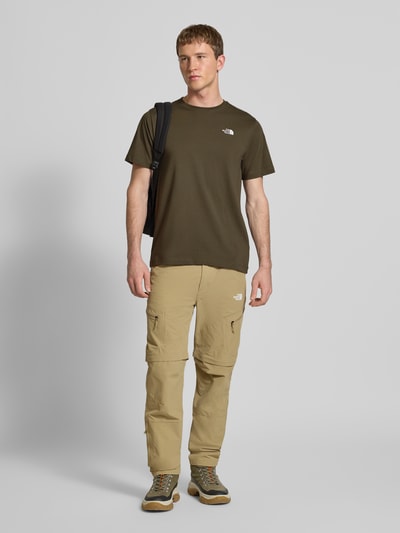 Männermodel trägt Regular Fit T-Shirt aus Baumwoll-Mix Modell 'EVOLUTION' von The North Face in Dunkelgrün mit Label-Detail, Ganzkörperansicht von vorne.