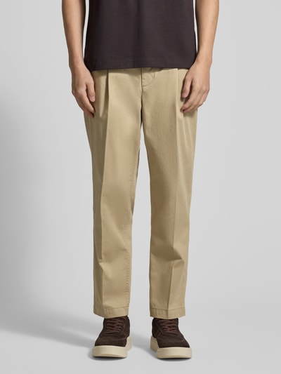 Männermodel trägt Regular Fit Chino aus Baumwoll-Mix Modell 'TAAMIR PLEATED' von Armedangels in Beige mit Logo-Stitching, Ganzkörperansicht von vorne.