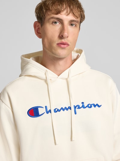 Männermodel trägt weißen Hoodie mit Label-Stitching von Champion aus Baumwoll-Mix, lockerer Schnitt, Nahaufnahme Oberkörper.