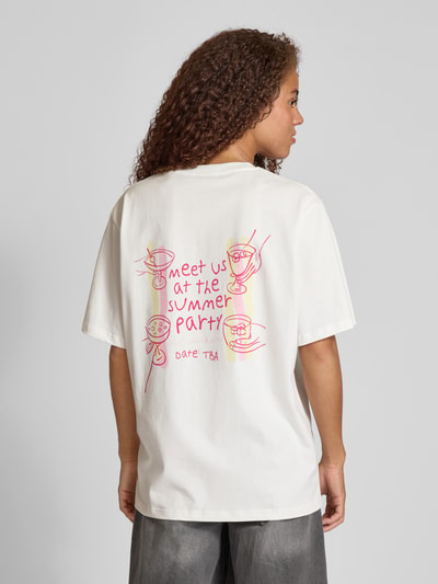 Frauenmodel trägt Oversized T-Shirt mit Label-Print von OH APRIL aus reiner Baumwolle, weiß mit pink-gelbem Print, Rückenlänge 69 cm, Ganzkörperansicht Rückansicht.