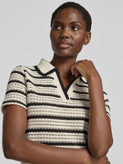 Frauenmodel trägt Strickshirt mit Polokragen Modell 'MIFFY' von MANGO aus cremefarbenem und schwarzem Material-Mix mit kurzen Ärmeln, Nahaufnahme Oberkörper.