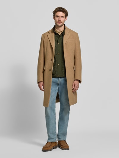 Mężczyzna nosi Regular Fit kamizelkę z naszywką z logo model 'BEATON' od Polo Ralph Lauren w odcieniach oliwkowej zieleni, beżowy płaszcz, jasnoniebieskie dżinsy, neutralna faktura, Ganzkörperansicht von vorne.