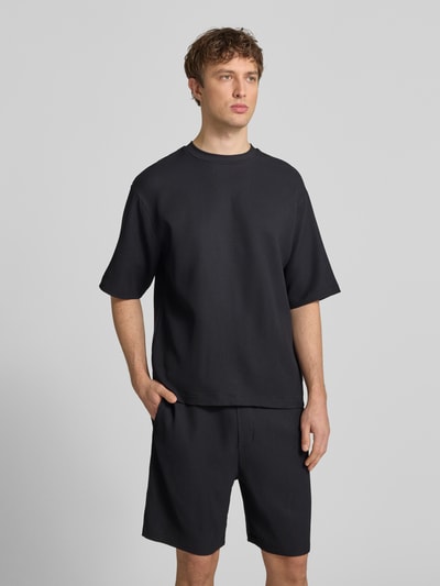 Männermodel trägt Regular-Fit T-Shirt in Plissee-Optik von REVIEW, schwarzer Material-Mix mit Stretch-Anteil, Rundhalsausschnitt, Ganzkörperansicht von vorne. Rückenlänge bei Größe M 68 cm.