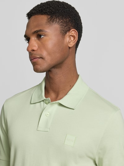 Männermodel trägt Slim Fit Poloshirt aus Baumwoll-Mix Modell 'PASSENGER' von BOSS Orange, Optik: Unifarben, Logo-Patch, Nahaufnahme Oberkörper.