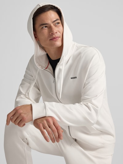 Männermodel trägt Relaxed Fit Sweatjacke aus reiner Baumwolle Modell 'DAPOZIP' von HUGO, weiß, Kapuze, Label Print, Nahaufnahme Oberkörper