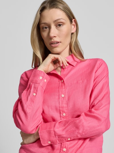 Modelka kobieca ma na sobie Regular Fit Leinenbluse mit Label-Stitching von Gant z lnu, krój regular fit, kołnierzyk koszulowy, wyhaftowane logo, listwa guzikowa, długość tyłu 66 cm w rozmiarze 36, długość rękawów 60 cm w rozmiarze 36, różowy kolor, gładka faktura, zbliżenie na górną część ciała