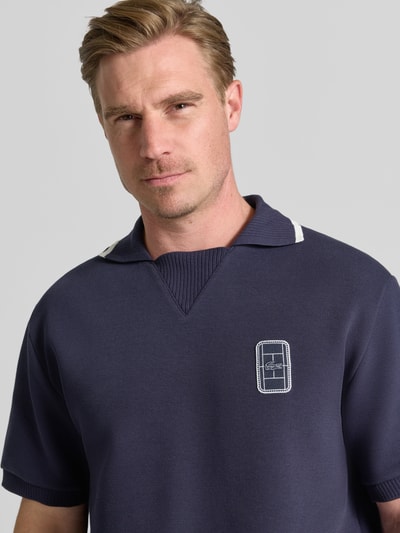 Mężczyzna nosi koszulkę polo o kroju loose fit Loose Fit Poloshirt od Lacoste, ciemnoniebieska, gładka faktura, widoczne logo, Nahaufnahme Oberkörper.