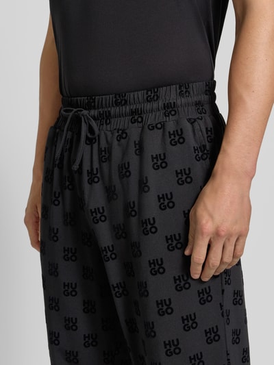 Männermodel trägt Regular Fit Sweathose aus Baumwoll-Mix von HUGO in Dunkelgrau mit schwarzem Logo-Muster, Nahaufnahme Oberkörper. Herren Sweathose von HUGO