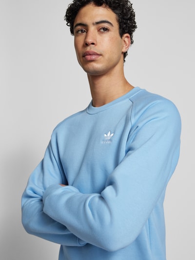 Männermodel trägt Sweatshirt mit Label-Stitching von adidas Originals in Hellblau, Baumwoll-Mix, lockerer Schnitt, Nahaufnahme Oberkörper.