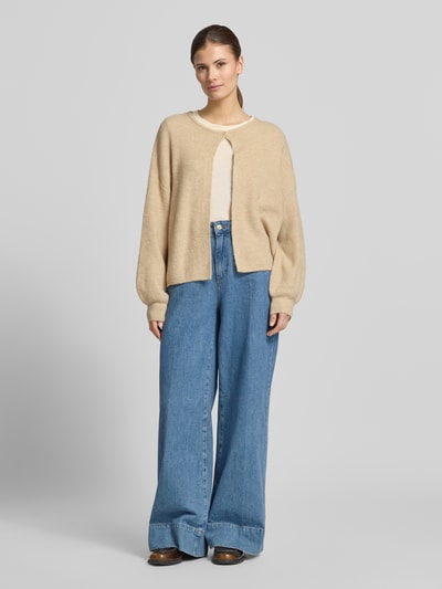Frauenmodel trägt Cardigan mit Knopfverschluss Modell 'Deriana' von OPUS in Beige, Woll-Mix, kombiniert mit weiter Jeans, Ganzkörperansicht von vorne.