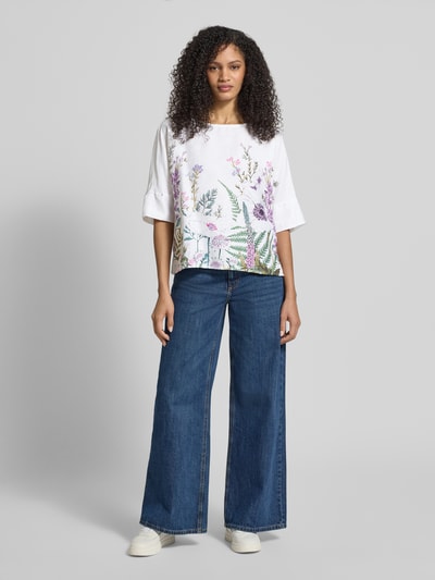Frauenmodel trägt Leinenbluse mit Halbarm und platziertem Blumenprint von Christian Berg Woman, reines Leinen, gerader Schnitt, U-Boot-Ausschnitt, Damen, Ganzkörperansicht von vorne.