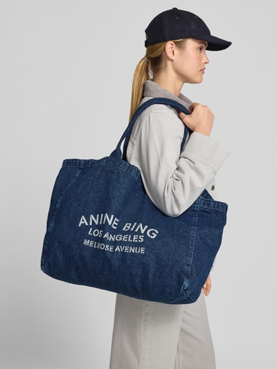 Frauenmodel trägt Tote Bag in Denim-Optik von Anine Bing mit Logo-Print, Reine Baumwolle, offenes Hauptfach, Schulterriemen, Ganzkörperansicht von vorne.