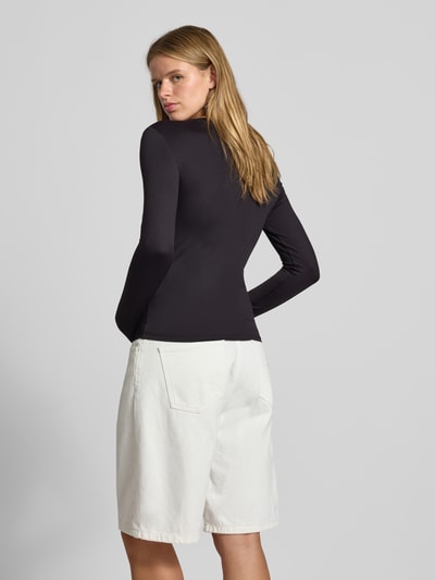 Vrouwenmodel draagt zwart shirt met lange mouwen en ronde hals, witte korte broek, Slim Fit Langarmshirt mit Rundhals-Ausschnitt Modell 'LULA' van PIECES, Ganzkörperansicht Rückansicht.