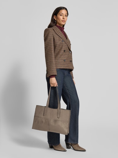 Vrouwenmodel draagt Shopper met Labeldetail model 'AMY' van LIEBESKIND BERLIN in taupe, met draagband en binnenvak met ritssluiting, hoofdvak met drukknoopsluiting, breedte 44 cm, lengte 28 cm, diepte 11 cm, lengte schouderband 61 cm, volledig zicht van voren.