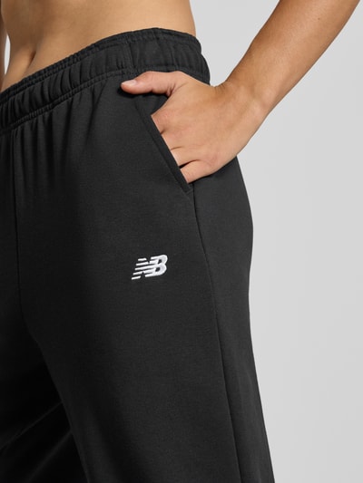 Männermodel trägt Regular Fit Sweatpants mit Logo-Stitching von New Balance, mieszanka bawełny, elastyczny pas, zakończenia nogawek:, wyhaftowane logo, czarne spodnie dresowe, Długość wewnętrzna nogawki w rozmiarze S: 74 cm, detailaufnahme.