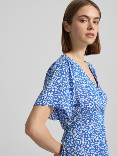 Frauenmodel trägt Minikleid aus reiner Viskose Modell 'EVIDA' von Only, Optik:Allover-Muster, Tailliert, Mini, V-Ausschnitt, Knopfleiste, Taillengürtel, Kurzarm, Material: reine Viskose, lebendige Blautöne mit weißen abstrakten Formen, glatte Textur, Nahaufnahme Oberkörper.