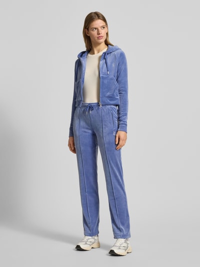 Frauenmodel trägt Juicy Couture Sweatjacke mit Kapuze Modell 'MADISON' aus Material-Mix mit Stretch-Anteil, Slim Fit, Tunnelzug, Reißverschluss, Eingrifftaschen und Label-Detail, Pastellblau, samtige Textur, Ganzkörperansicht von vorne.