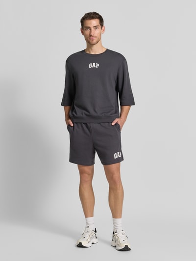 Männermodel trägt Straight Fit Shorts mit Logo-Stitching Modell 'Arch' von GAP in Dunkelgrau, Baumwoll-Mix, Ganzkörperansicht von vorne.