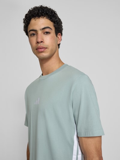 Männermodel trägt Regular Fit T-Shirt aus reiner Baumwolle von adidas Sportswear, Optik: Unifarben, Logo-Stitching, Kontraststreifen, Rundhals, Kurzarm, Nahaufnahme Oberkörper.