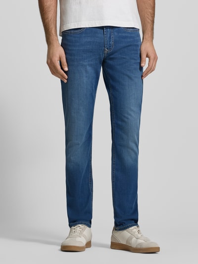 Männermodel trägt Straight Fit Jeans aus Baumwoll-Mix von MAC in mittelblau mit 5-pocket-design, label-patch, contrastnaden, ganzkörperansicht von vorne.
