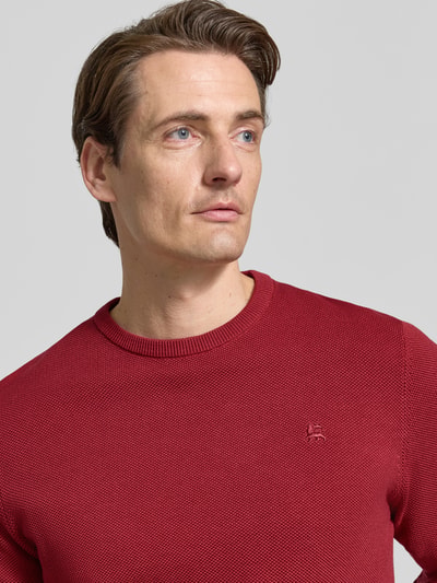 Männermodel trägt Regular Fit Strickpullover aus reiner Baumwolle mit Label-Detail von LERROS in Rot, texturierte Oberfläche, Nahaufnahme Oberkörper. Rückenlänge 68 cm, Ärmellänge 69 cm, elastische Abschlüsse.