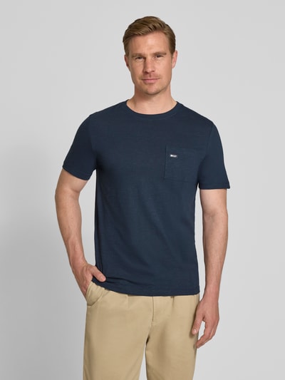 Męski model nosi Regular Fit T-Shirt aus reiner Baumwolle von s.Oliver RED LABEL, granatowy, materiał melanż, krótki rękaw, okrągły dekolt, kieszonka na piersi, label patch, widok całej sylwetki z przodu.